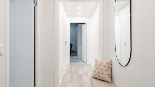 A hallway with a light-colored floor, a door on the left, and a large mirror on the right. - Spacious Apartment with Prime Location (Jyväskylä)