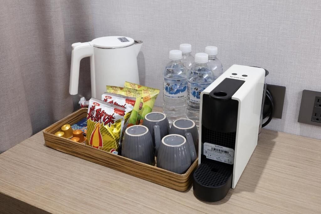 A tray with snacks, water bottles, a kettle, and a coffee machine on a table.