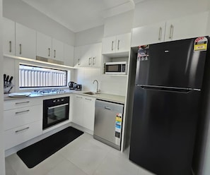 A modern kitchen with white cabinets, a black refrigerator, a microwave, a stove, and a dishwasher. - RedFlames Retreat@Gables/BoxHill/Marayla/RouseHill (Gables)