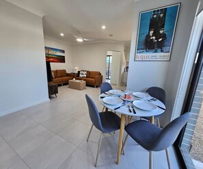 A modern living room with a dining area, a painting on the wall, and a poster of the Beatles.