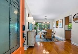 A modern interior with a dining area, wooden flooring, and a view through a glass door.