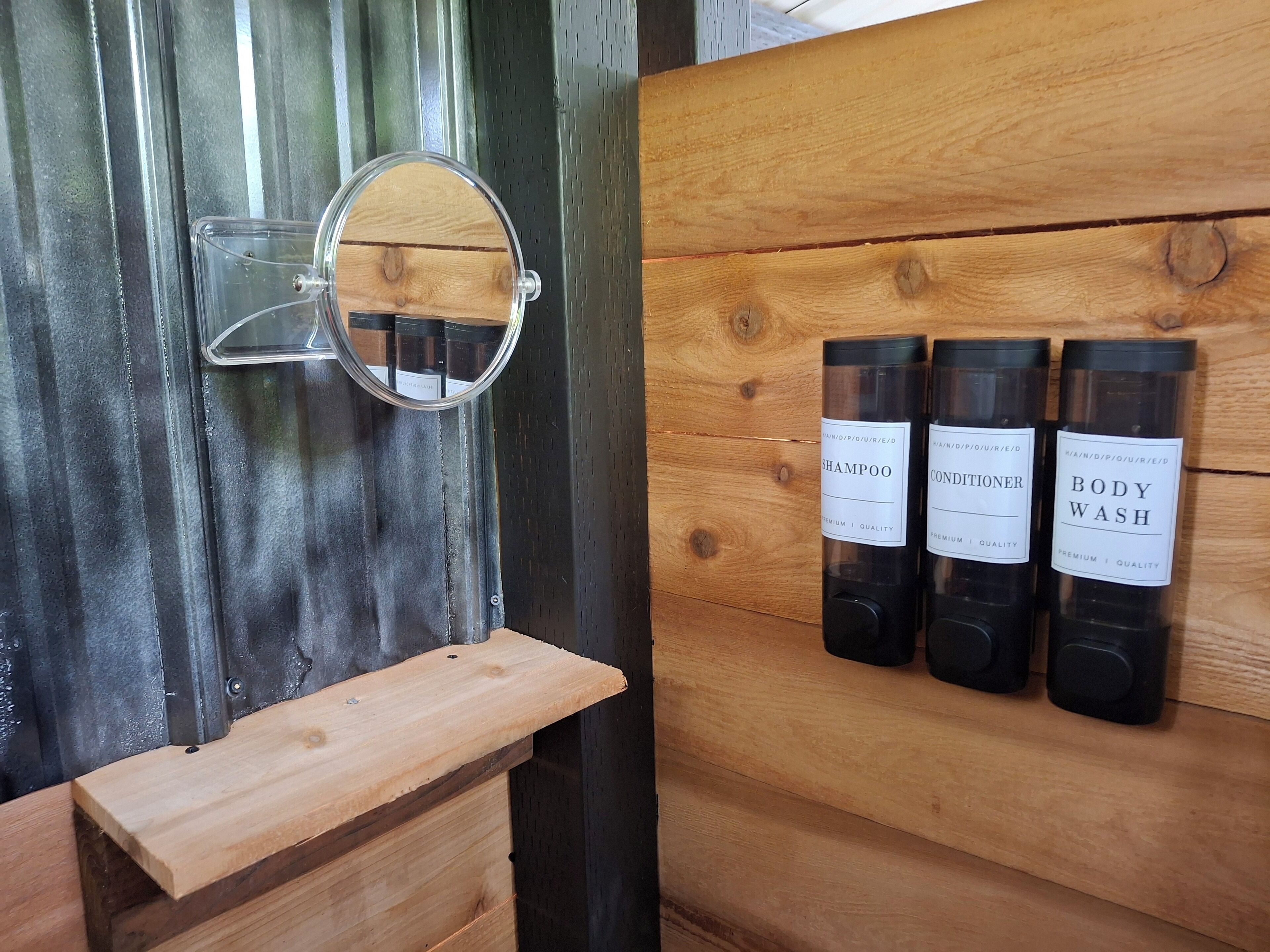 Un baño con tocador de madera, un espejo y tres botellas de champú, acondicionador y gel de baño.