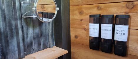 Un baño con tocador de madera, un espejo y tres botellas de champú, acondicionador y gel de baño.
