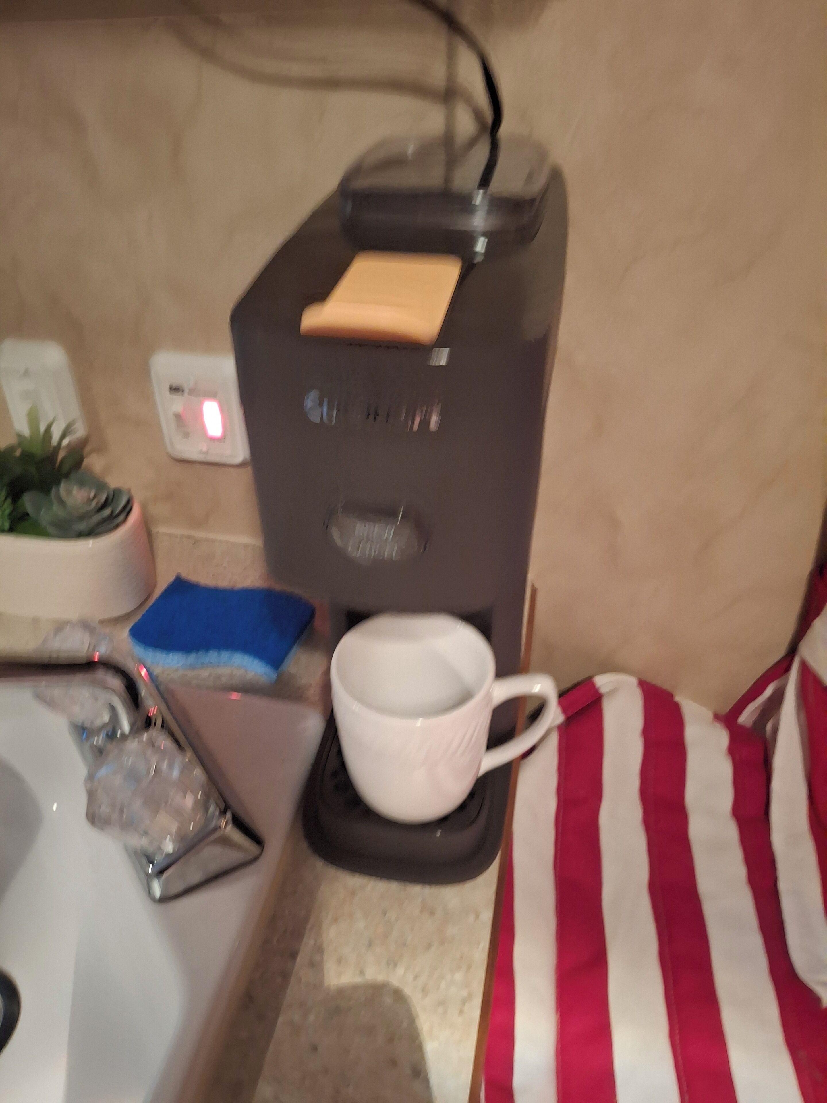 Una cafetera con un portavasos, un enchufe y una planta pequeña en la encimera.