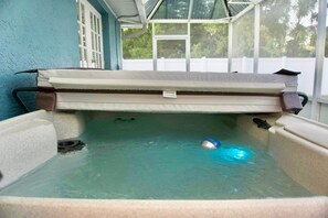 A hot tub with a cover, a drain, and a blue object floating in the water.