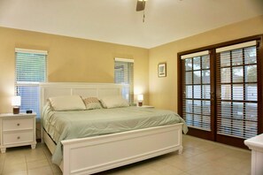 A bedroom with a bed, bedside tables, a nightstand, a window with blinds, and a door with a view.