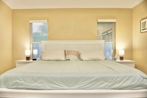 A hotel room with a large bed, two bedside tables with lamps, and a window with blinds.