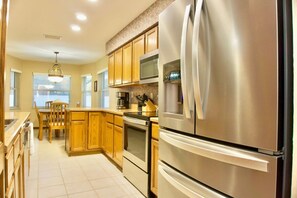 A modern kitchen with stainless steel appliances, wooden cabinets, and a dining area with a chair.