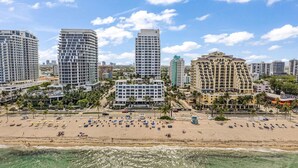 A beachfront hotel with multiple floors, a sandy beach with umbrellas, and a clear view of the ocean. - Gorgeous Jr Suite on Pool and Lanai Level of Hotel (Fort Lauderdale)