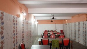 A dining area with multiple tables and chairs, a ceiling fan, and patterned walls. - Hotel Aishwarya New Digha (Digha)