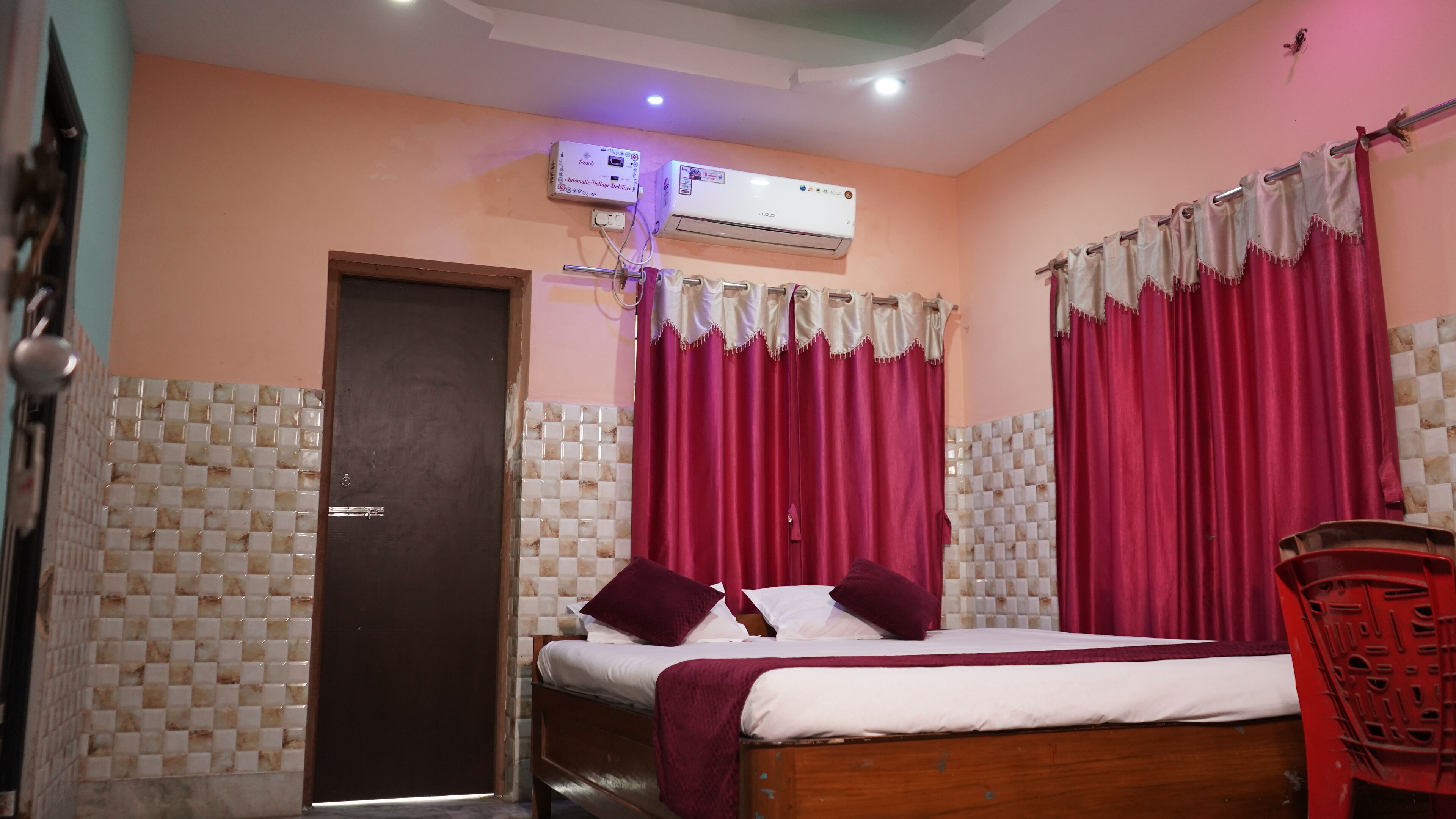 A room with a bed, a door, an air conditioning unit, and curtains.