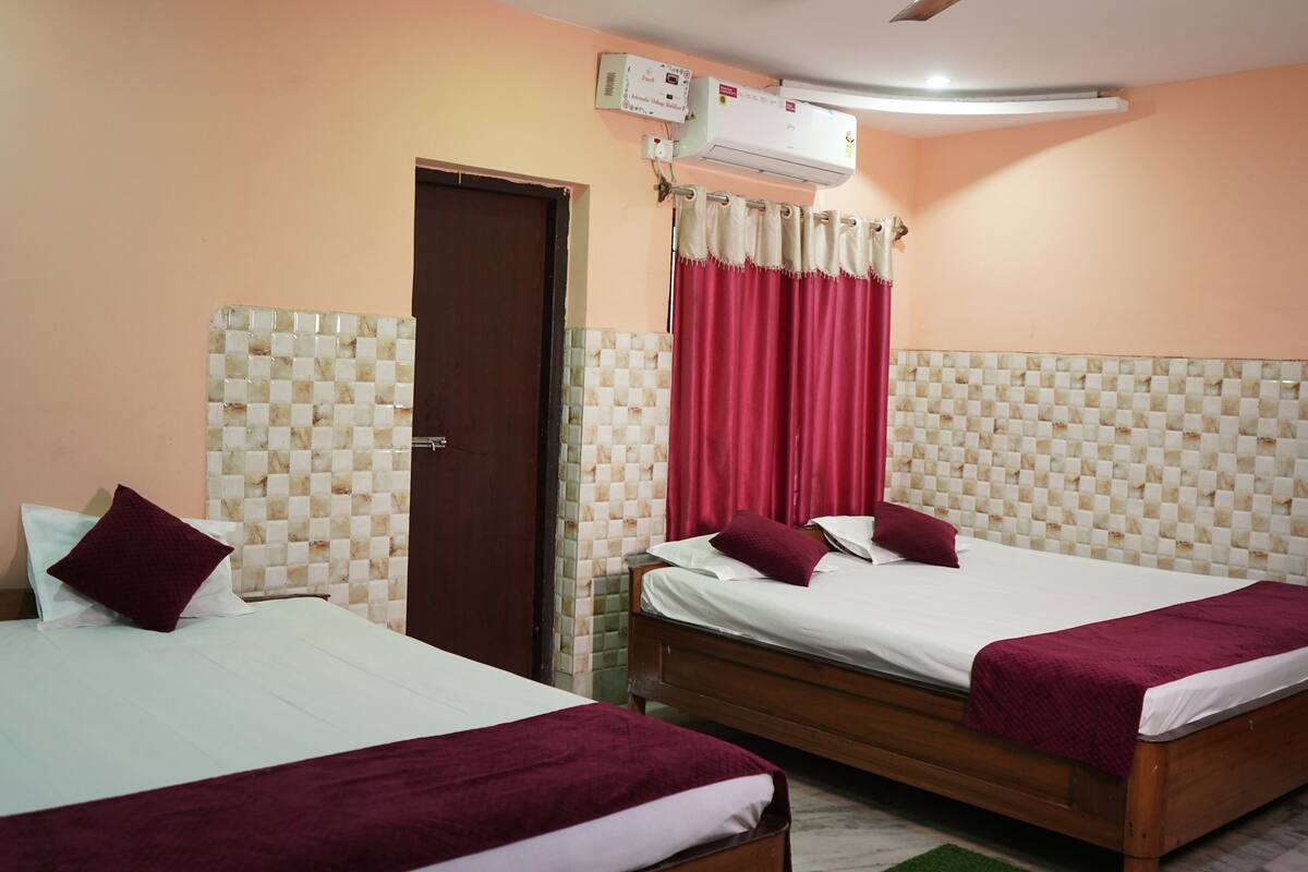 Een hotelkamer met twee bedden, een plafondventilator, een airconditioning en een raam met rode gordijnen.
