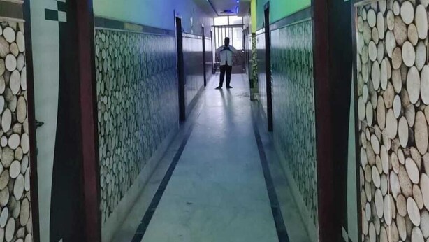 A hallway with a patterned wall, a person walking, and a door with a sign. - Hotel Aishwarya New Digha (Digha)