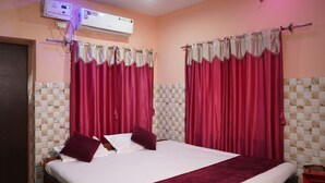 A hotel room with a bed, two pillows, a red blanket, a window with pink curtains, a wall-mounted air conditioner, and a tiled wall. - Hotel Aishwarya New Digha (Digha)