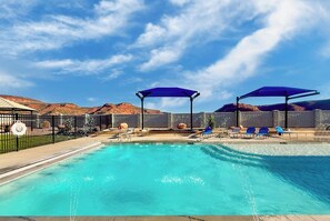 Una piscina amb ombrelles blaves, gandules i una zona tancada amb un paisatge desèrtic al fons.