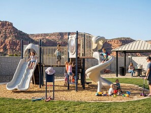 A playground with slides and climbing structures, surrounded by a landscaped area with a clear view of a mountainous landscape.