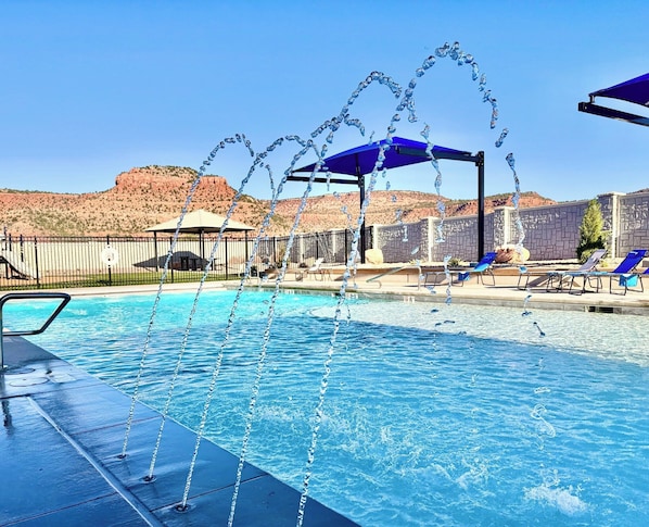 A pool with water jets, lounge chairs, and a view of red rock hills.