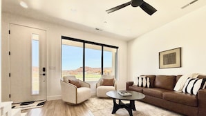 Un salón amplio con un gran ventanal, un ventilador de techo y un sofá de cuero marrón.
