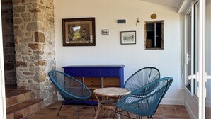 A patio with a stone wall, a blue sofa, two blue chairs, and a small table. - Waterfront house with large walled garden (Île-aux-Moines)