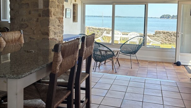 A dining area with stone walls, a large window, and a view of the sea. - Waterfront house with large walled garden (Île-aux-Moines)