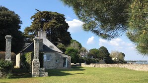 A stone house with a chimney, surrounded by a grassy yard and a stone wall. - Waterfront house with large walled garden (Île-aux-Moines)