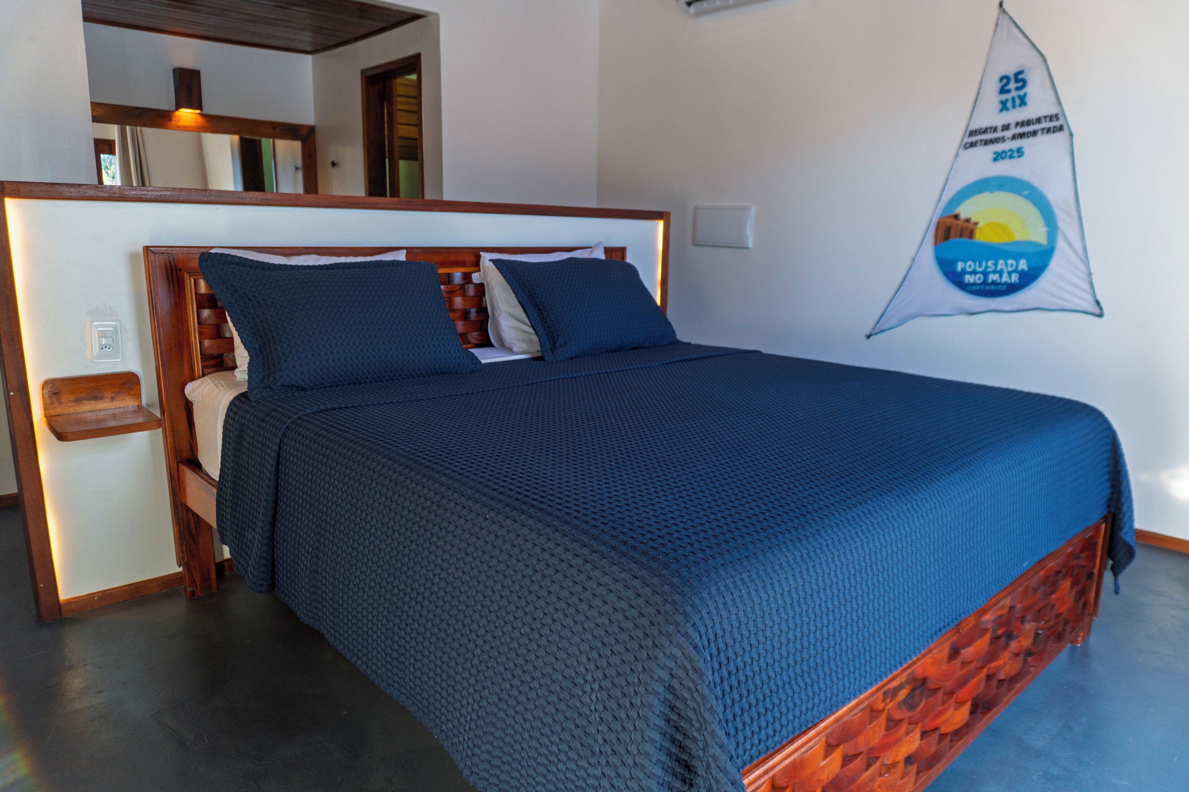 A neatly made bed with a blue bedspread and pillows, a wooden headboard, and a wall-mounted flag.