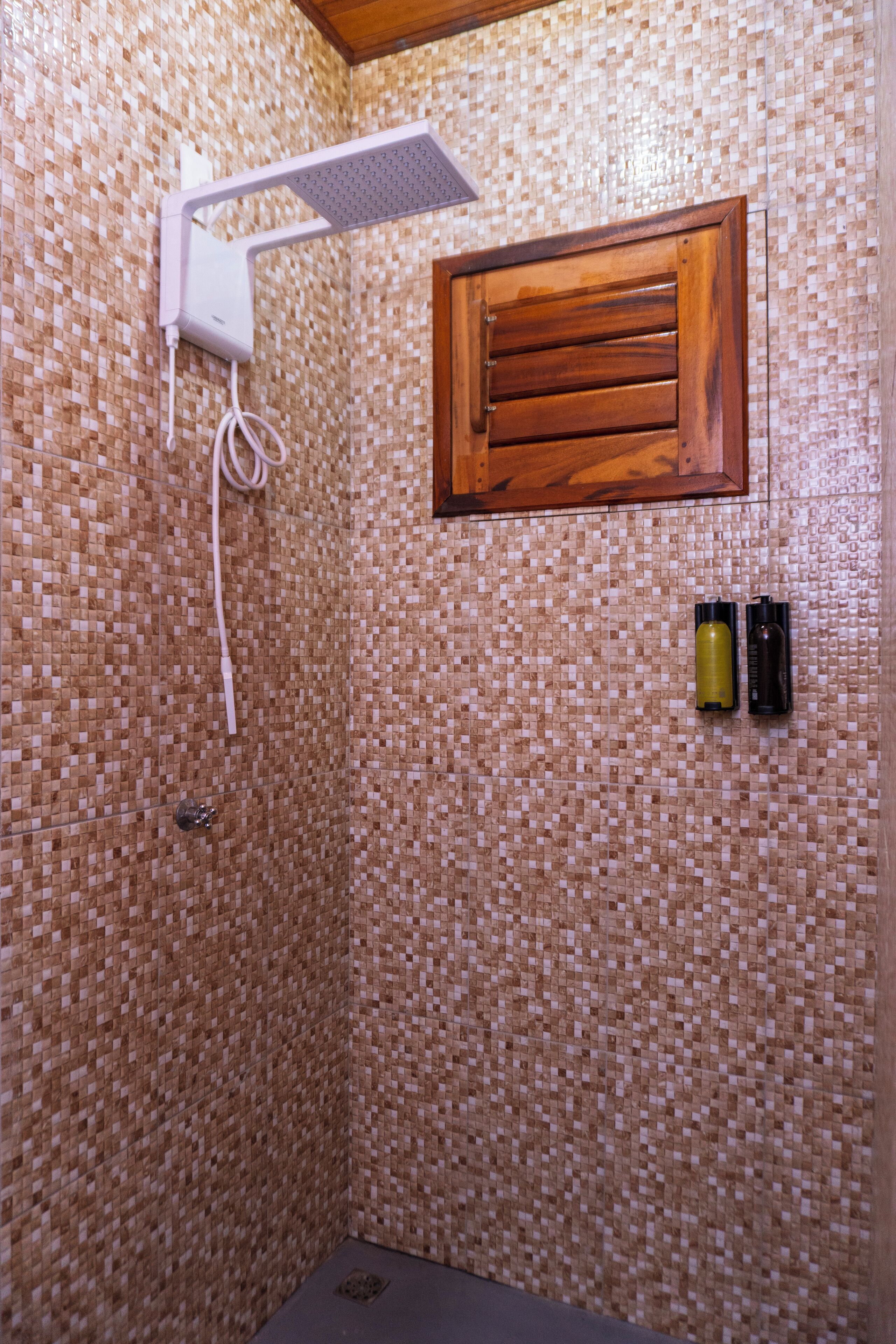 Eine Dusche mit gefliesten Wänden, einem Holzfenster und zwei Flaschen an der Wand.