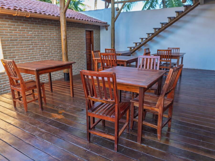 Una terraza de madera con mesas y sillas, un muro de ladrillo y una escalera.