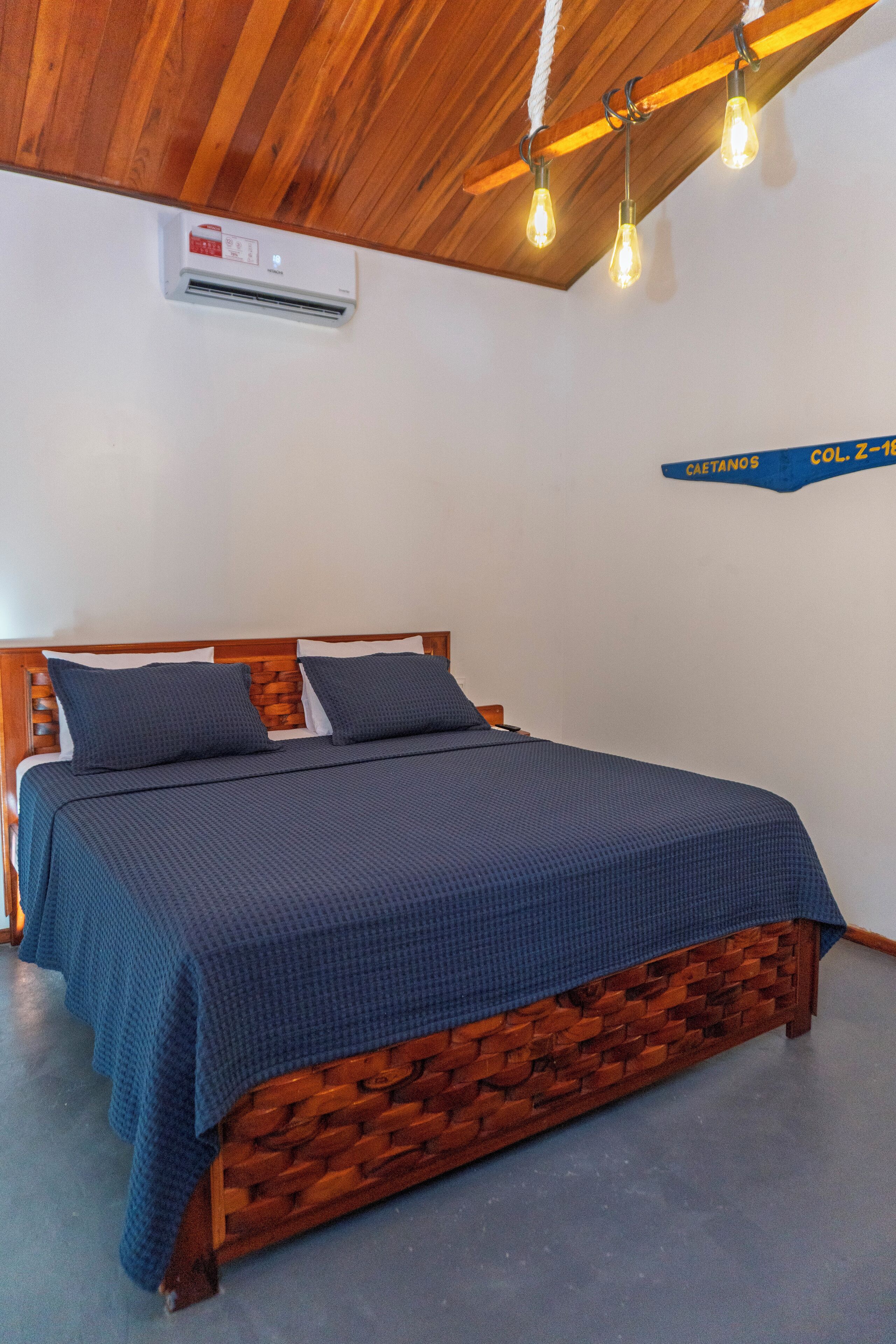 A bed with a wooden headboard, a blue bedspread, and a wall-mounted air conditioning unit.
