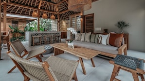 A spacious living area with a wooden ceiling, woven furniture, and a central table.