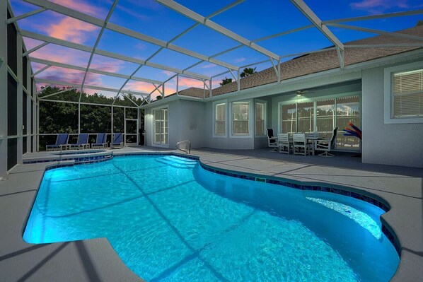 A swimming pool with a glass enclosure, sun loungers, and a patio area with a table and chairs.