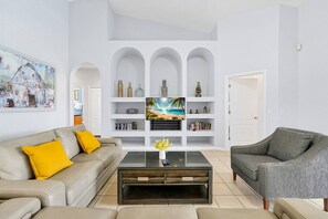 A living room with a sofa, armchair, coffee table, TV, and shelving unit.