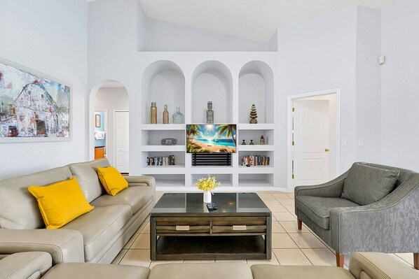 A living room with a sofa, armchair, coffee table, TV, and shelving unit.