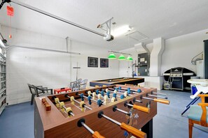 A room with a foosball table, a grill, and a billiards table.