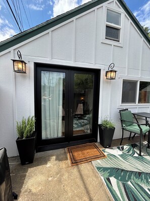 A house with a black-framed sliding glass door, two black wall-mounted lanterns, a green chair, and a small table. - Burrow on 24th - Hot Tub 1BR/1BA (Boise)