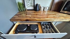 Uma cozinha com bancada de madeira, cafeteira e gaveta com utensílios.