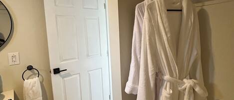 Un baño con una puerta blanca, un perchero con una toalla blanca y un albornoz blanco colgado en un perchero negro.