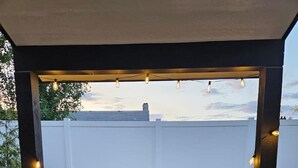 Un espace patio avec deux chaises et une table, une petite plante en pot et des guirlandes lumineuses.