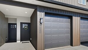Un garage moderne avec une grande porte grise et une petite porte d’entrée ornée d’une guirlande.