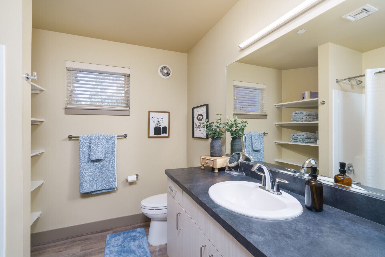 Un baño moderno con un espejo grande, un lavabo y un inodoro. Hay toallas en la pared y un estante pequeño con artículos de aseo.
