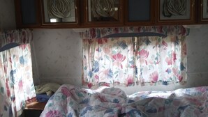 A room with a bed, floral curtains, and three framed artworks above the bed.