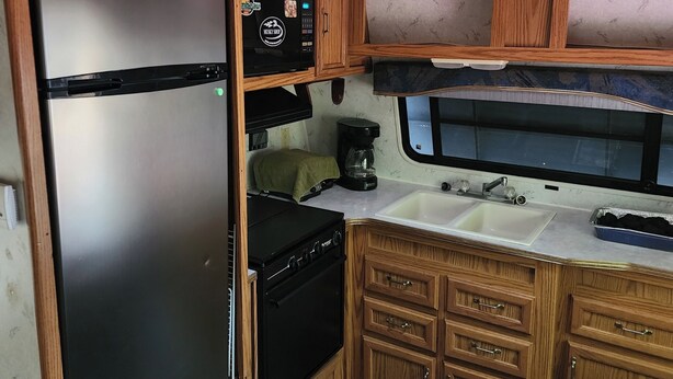 A compact kitchen with a black refrigerator, wooden cabinets, a microwave, and a sink.