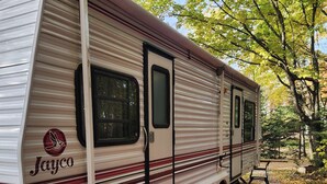 A Jayco RV parked in a wooded area with a red mat on the ground.