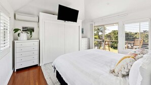 A bedroom with a bed, a TV mounted on a cabinet, a dresser, and a window with a view of greenery.