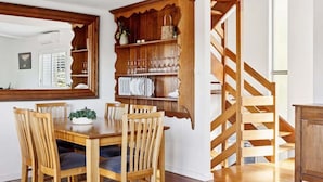 A dining area with a wooden table and chairs, a built-in bookshelf, and a wooden staircase.