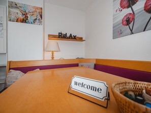 Ein Zimmer mit einem Holztisch, einem Schild mit der Aufschrift 'welcome', einer Lampe, einem Regal mit der Aufschrift 'RELAX' und Bildern an den Wänden.