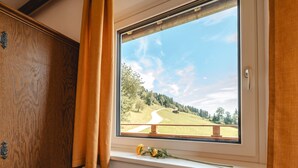 A room with a large window overlooking a scenic landscape, a radiator below, and wooden paneling on the left. - Panoramaperle by Interhome (Neukirchen am Großvenediger)