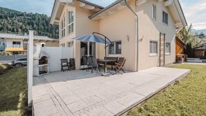 Une maison à deux étages dotée d’un patio, d’un espace salon extérieur et d’un barbecue.