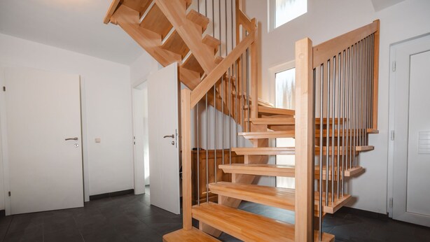 Un intérieur moderne avec un escalier en colimaçon en bois, un sol carrelé foncé et des murs blancs.