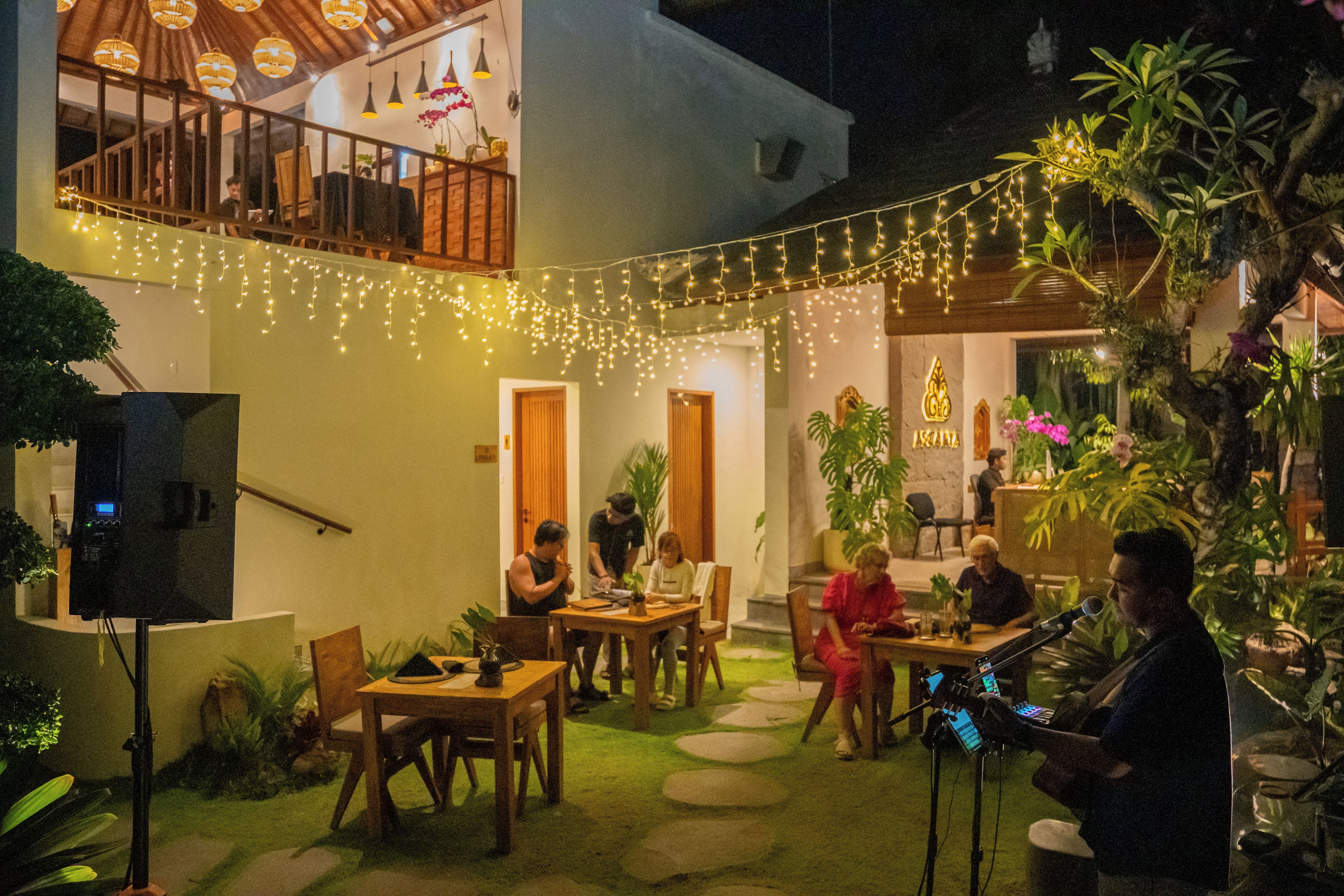 An outdoor seating area with tables and chairs, string lights, and potted plants.